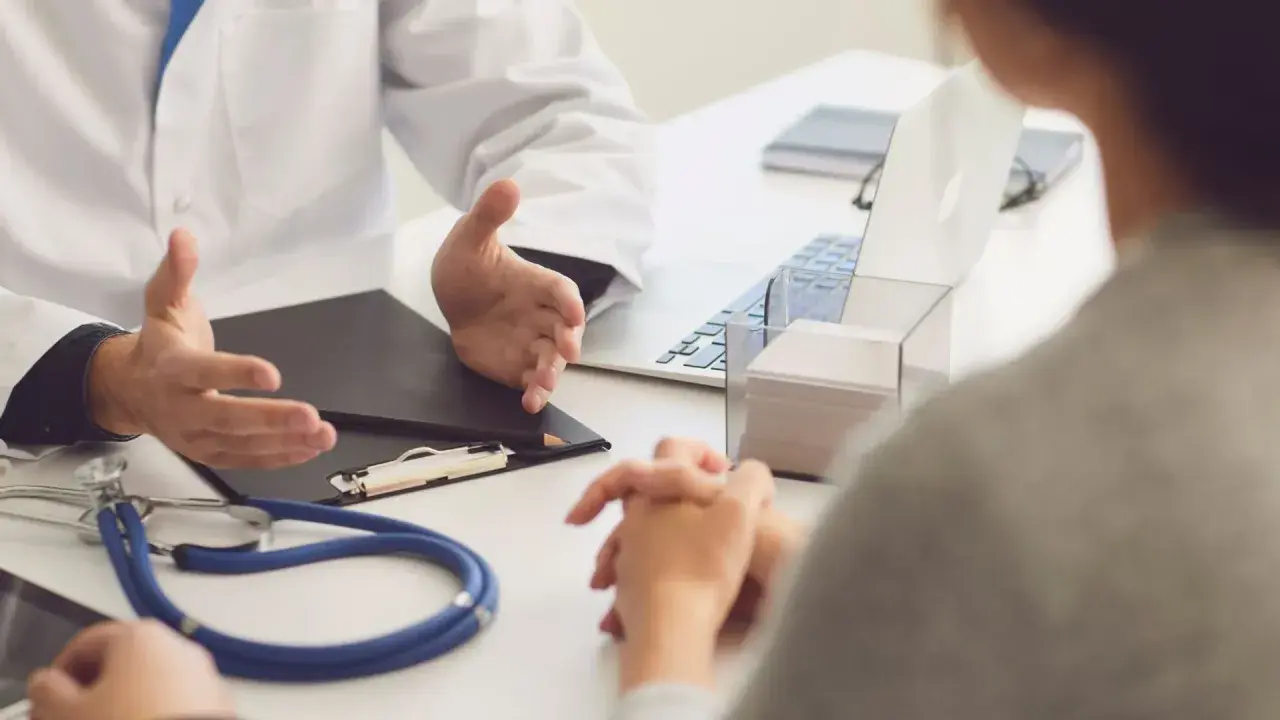 Lekarz omawia z pacjentem diagnozę, być może f43 kod choroby, przy biurku ze stetoskopem i laptopem.