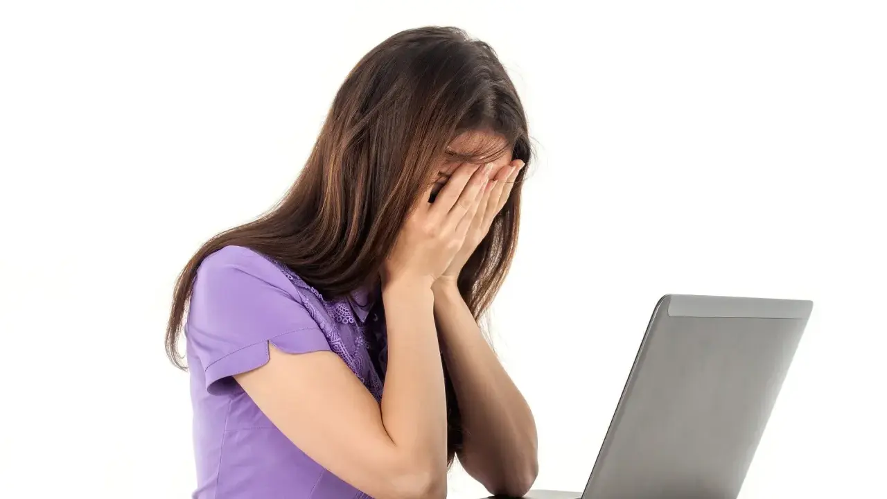 Kobieta zapatrzona w ekran laptopa, zakrywająca twarz dłońmi, emanuje apatią.