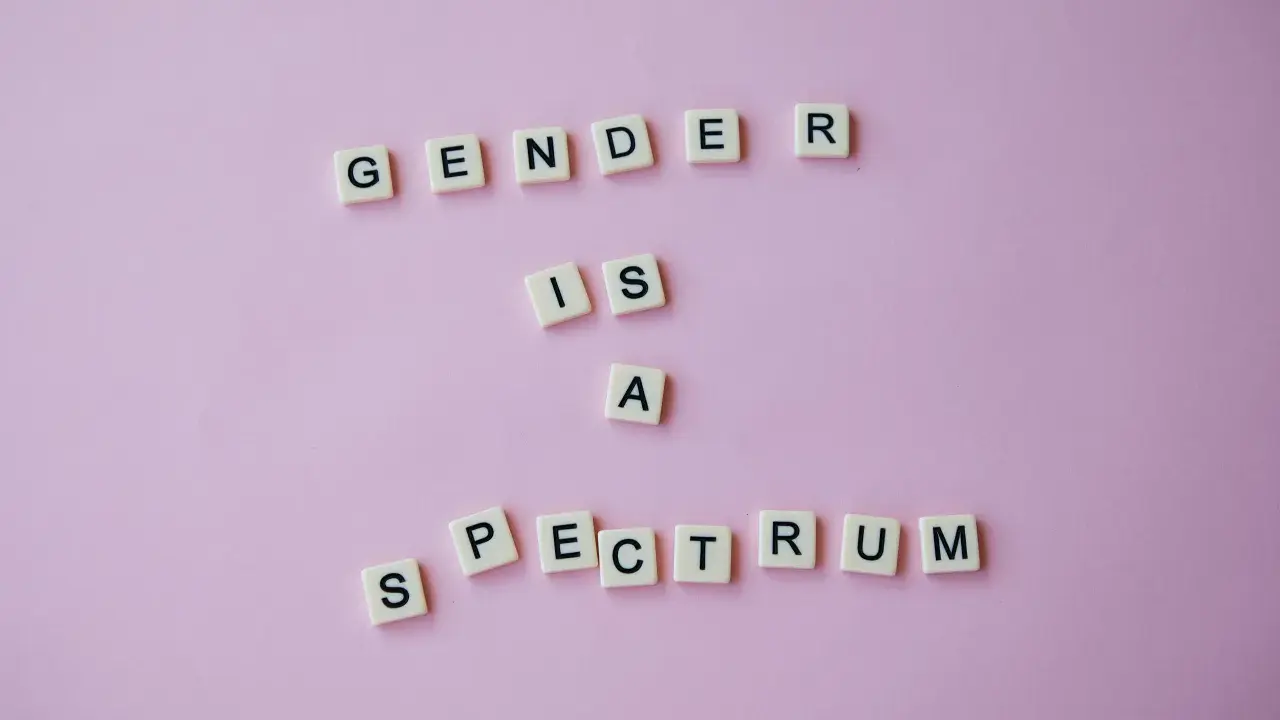 Litery na różowym tle układają się w napis "GENDER IS A SPECTRUM". To przypomnienie, że tożsamość płciowa nie jest binarna, a doświadczenie dysforii płciowej jest częścią tej złożoności.
