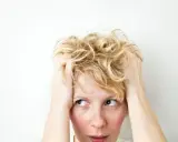 Kobieta z blond włosami wplata dłonie we włosy, jej wyraz twarzy sugeruje wahania nastroju i niepokój.