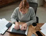Kobieta pracuje przy laptopie, analizując dokumenty. Zastanawia się, czy umowa zlecenie wlicza się do stażu pracy, szukając odpowiedzi online.