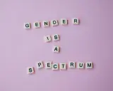 Litery na różowym tle układają się w napis "GENDER IS A SPECTRUM". To przypomnienie, że tożsamość płciowa nie jest binarna, a doświadczenie dysforii płciowej jest częścią tej złożoności.