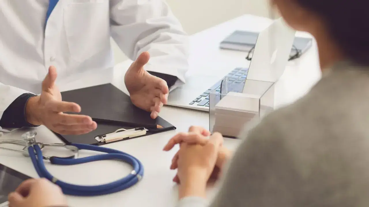 Lekarz omawia z pacjentem diagnozę, być może f43 kod choroby, przy biurku ze stetoskopem i laptopem.