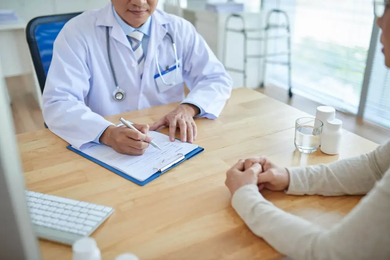 Lekarz notuje objawy pacjenta, który czeka na diagnozę. Na stole leki i szklanka wody. Może to być f41 kod choroby.